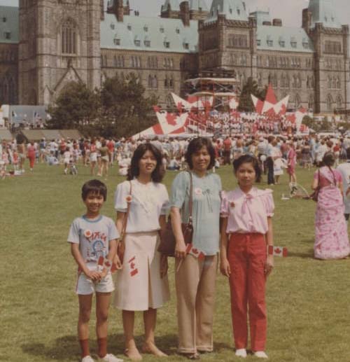 Four people with Canada flags in front of the Parliament building.